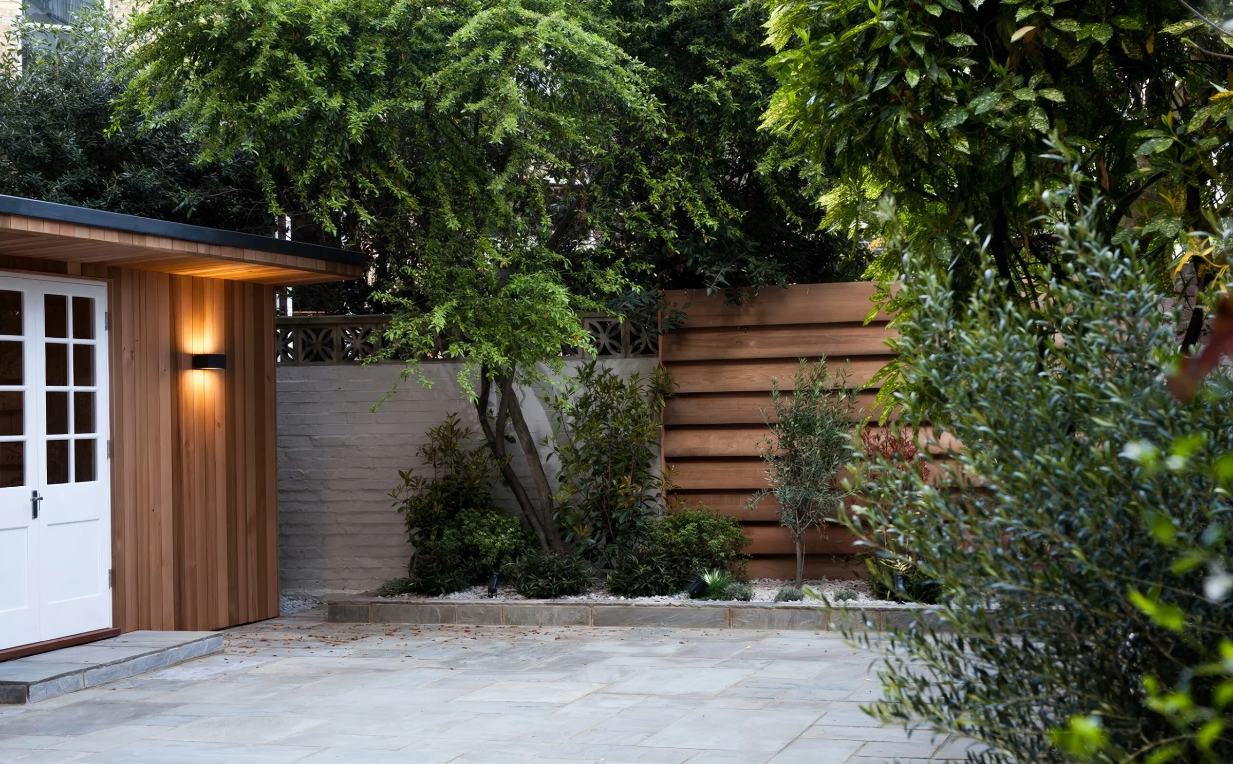 Cedar clad garden room with warm wall lights in a London courtyard garden