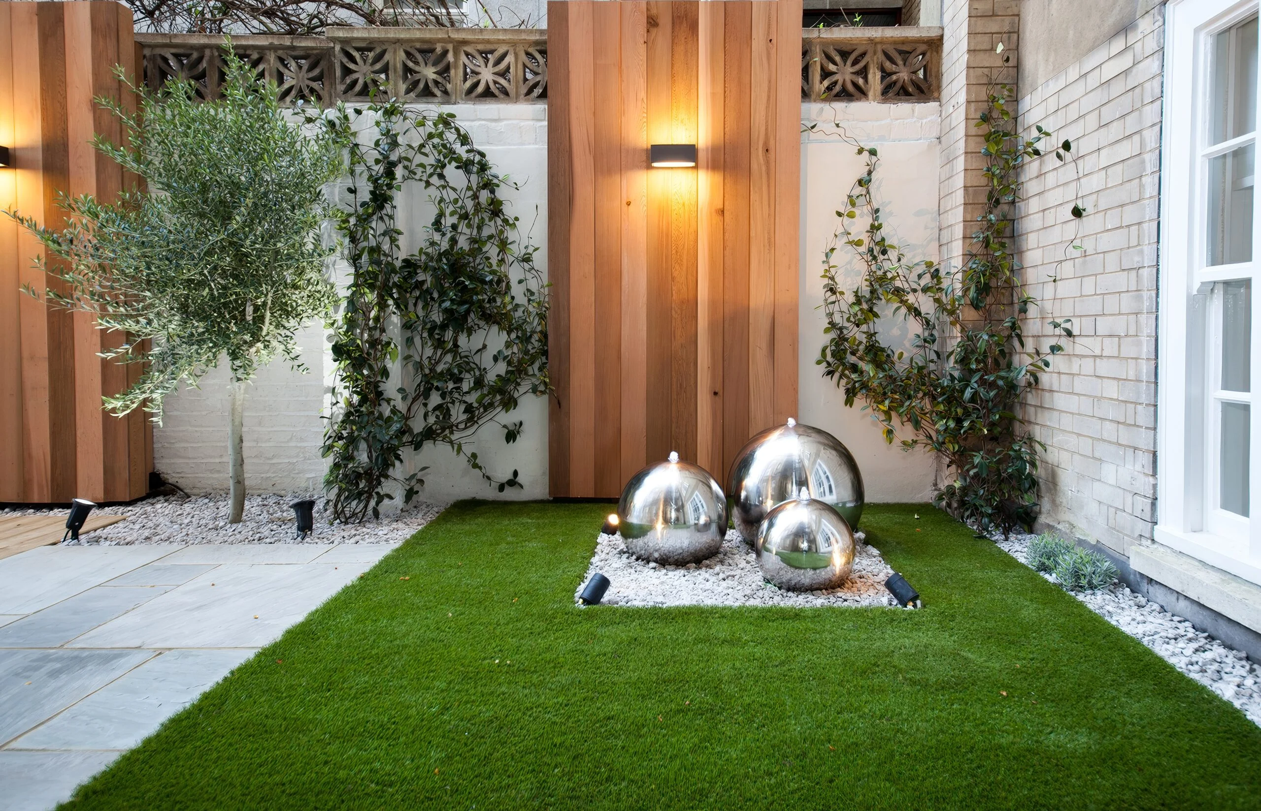 Stainless steel sphere water feature on a lawn framed by cedar panels
